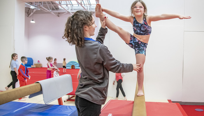 girl balancing on beam with coach assistance 