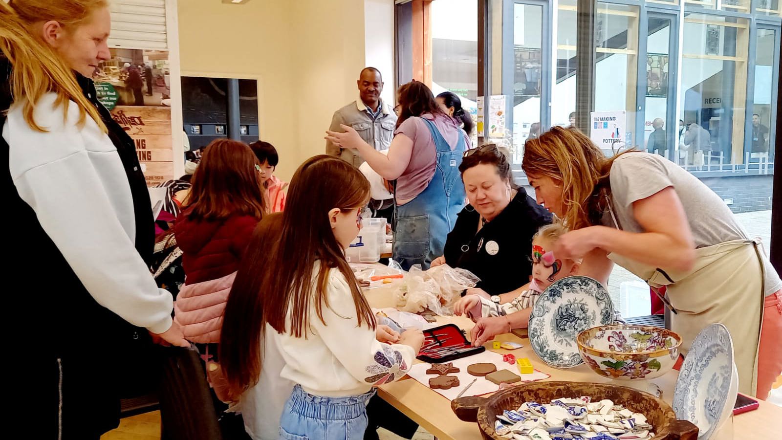 A crowd of people grouped round a table covered in craft materials and ceramics