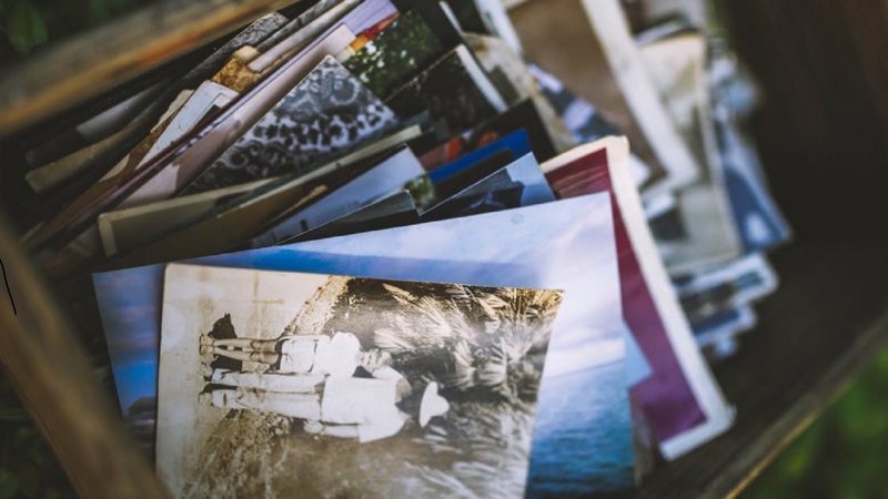 Selection of old photos and postcards in a box. The first one shows a sepia coloured image of an older person with a hat with their arm round a child.