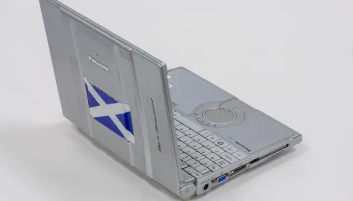 a photograph of a grey laptop. On the lid, there is a Scottish flag sticker.