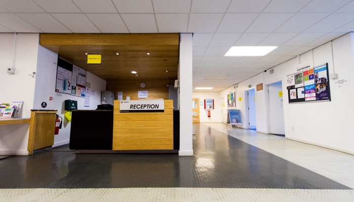 A spacious entrance area to Barmulloch Community Hub. The reception is covered. The floor is black and white