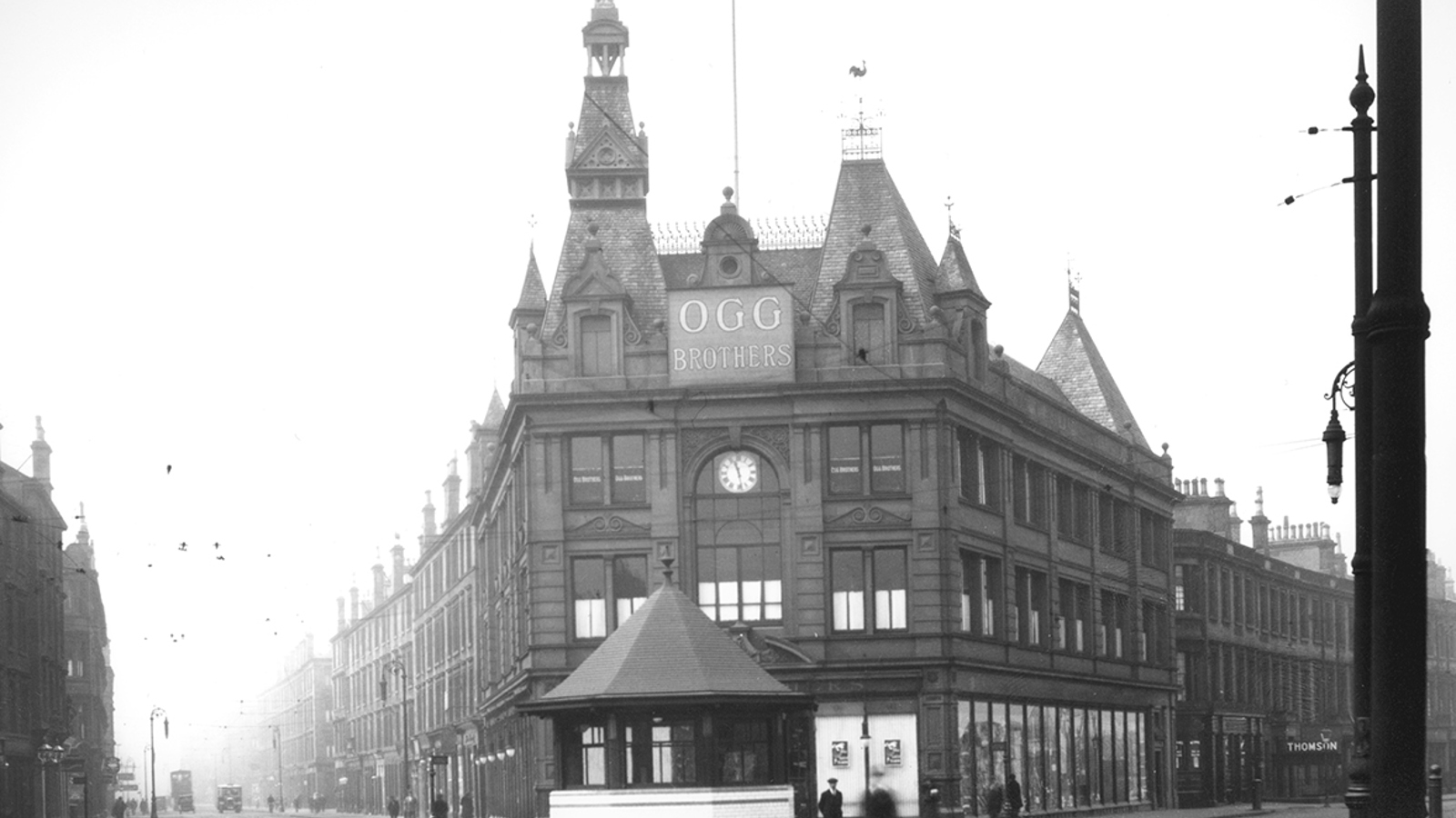 A black and white photograph of a large sandstone building on the corner of a cobbled street with tram lines.