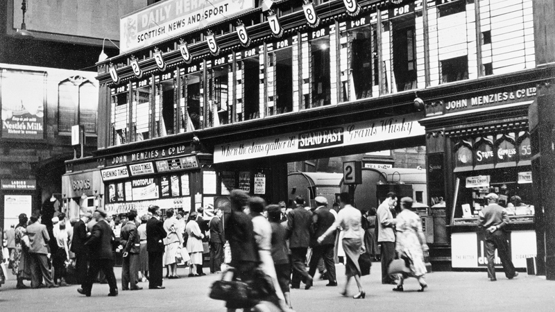 Black and white photograph showing passengers walking across the concourse at St Enoch station, in 1955.