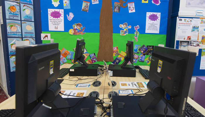 Children's PC area with 4 computers facing each other. On the wall beside them there is home-made children's tree artwork