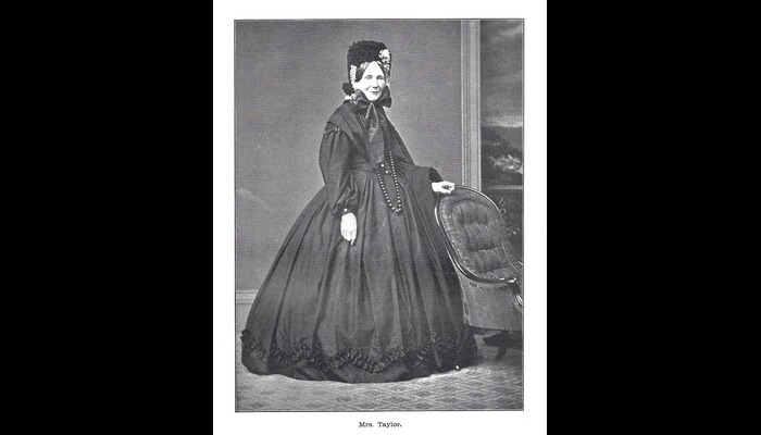 Photograph of a standing lady in Victorian clothing. A dress with a large skirt.