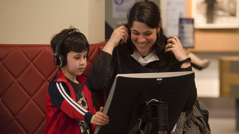 An adult and child viewing a computer with headphones on and smiling