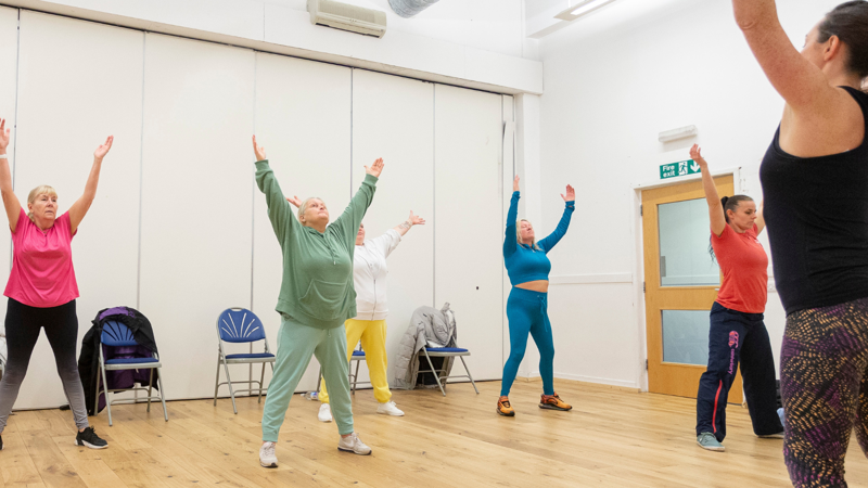 A group of people and an instructor with their hands in the air while taking part in a wellbeing class