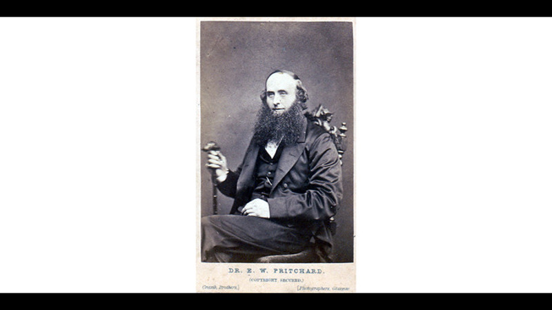 A photograph of a seated man with a beard