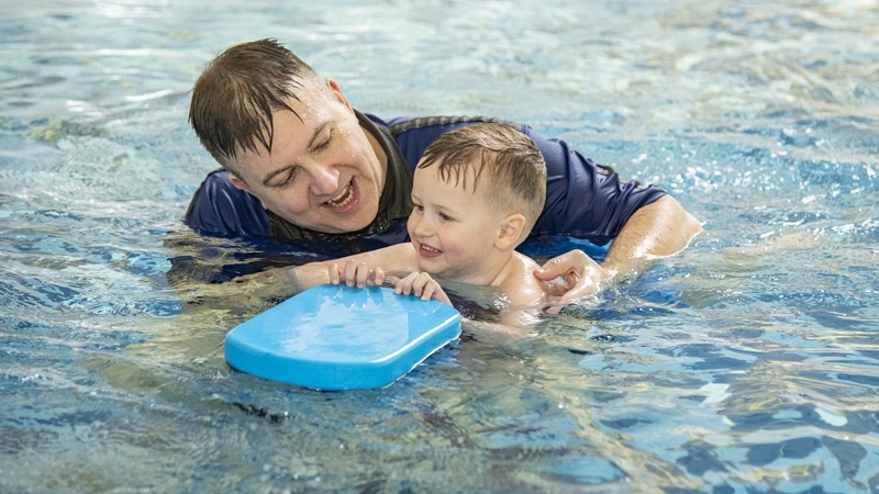 A swimming coach helping a child in the pool who is holding a float