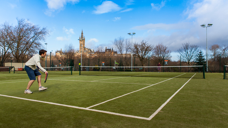 A person hitting a tennis ball on the courts at Kelvingrove Park