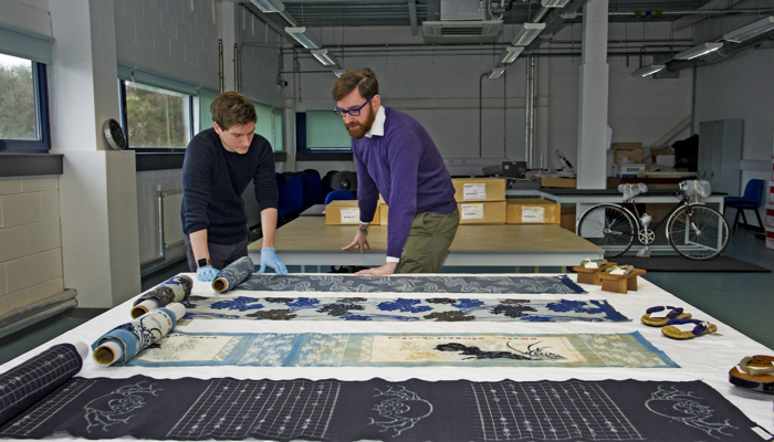 Two curators at work in the Research Room at GMRC viewing textile objects laid flat on a table