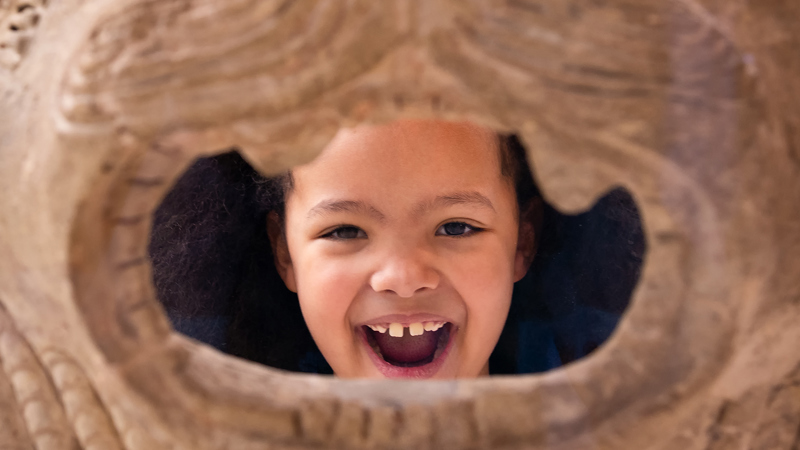 Young girl visitor peeking through object with big smile at The Burrell Collection