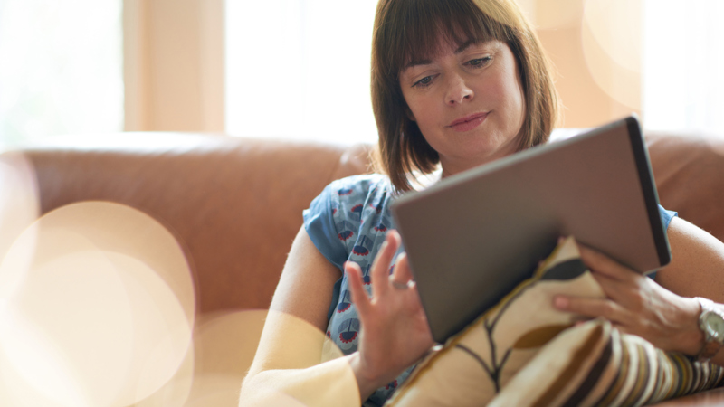 A person sitting on a sofa holding an electronic tablet