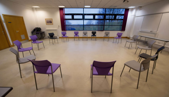 Chairs are set out in a circle in a room with a wooden floor. There is a window in the background.