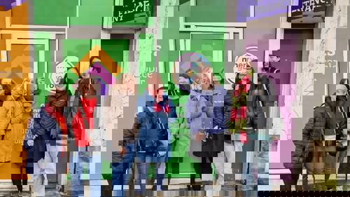 A group of six people outside a colourful shop front