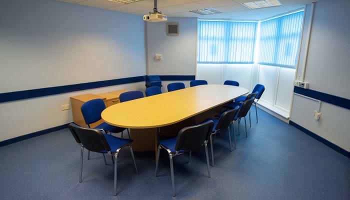 round wooden table with blue chairs round it ready for a meeting