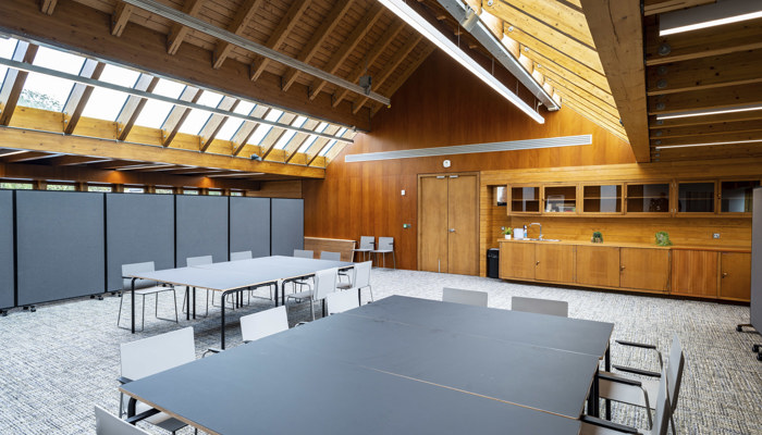 large meeting space with two large tables with chairs round them. the room has windows up high with wooden panelling across the roof