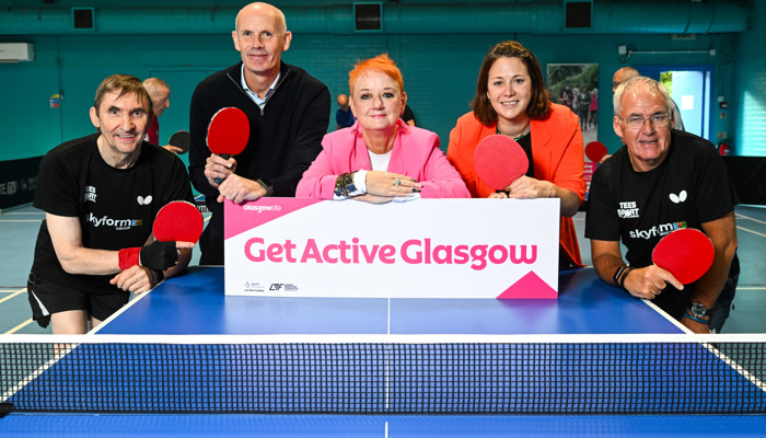 Men and women stand at the end of a table tennis table with a sign which reads 'Get Active Glasgow'