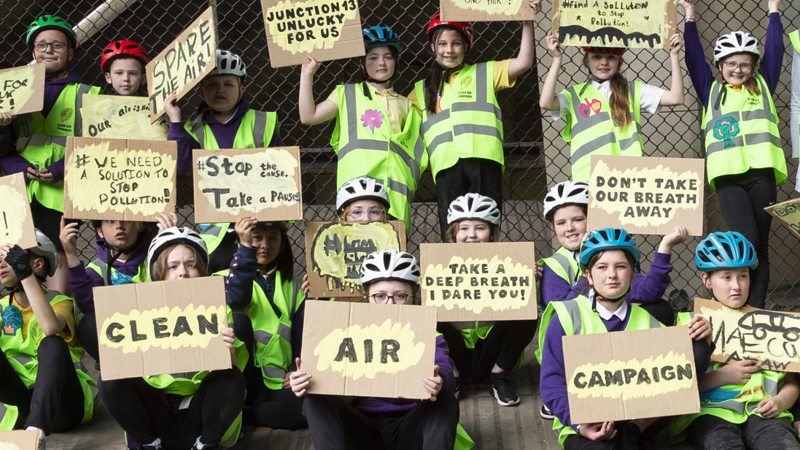 Children in cycling helmets pose together holding a variety of anti-pollution signs