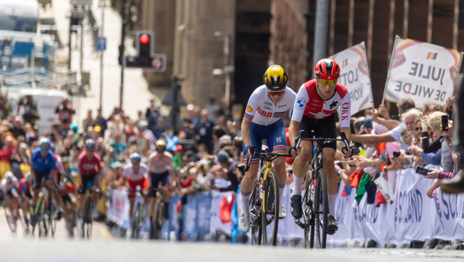 Cyclists racing up the hill on Montrose Street in Glasgow during the 2023 UCI Cycling World Championships in front of cheering crowds of people.