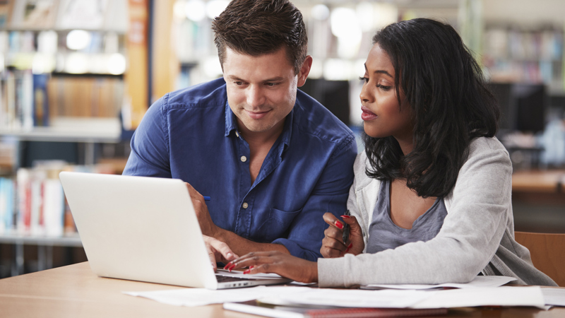 Two people are in a library working together on a laptop.