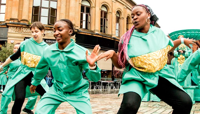 A group of contemporary dancers perform outdoors outside Merchant Square in Glasgow city centre. The dancers have different outfits but all wear mainly pale green with black and trainers.
