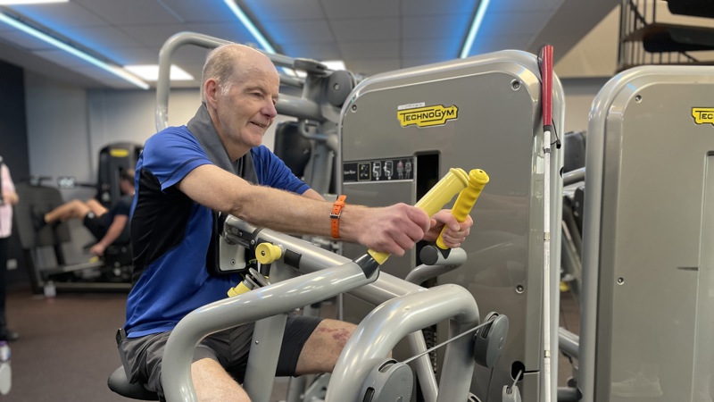 Glasgow Club member Raymond Ward using a low row back machine at Glasgow Club Tollcross gym. They have their arms out in front of them holding onto the handles of the machine.