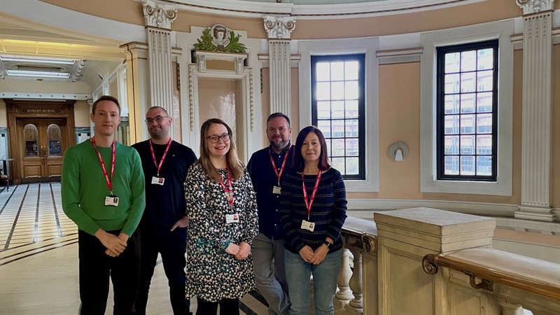 A group of five adults stand in the Mitchell Library.