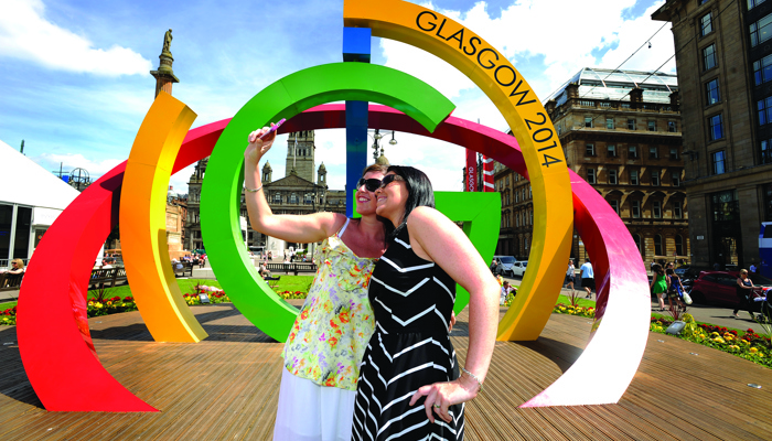 Two people taking a selfie on a sunny day in George Square in front of the Big G sculpture.