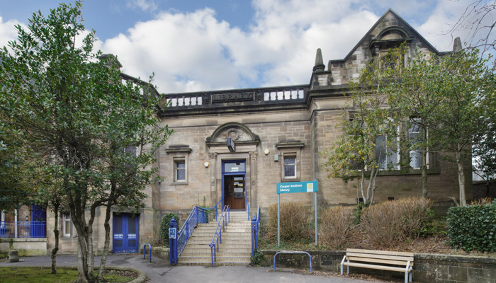 Exterior of Couper Institute Library. There are steps to the entrance, trees and a bench.