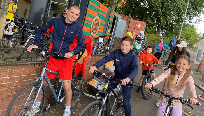 An adult and two children on bikes at Drumchapel Cycle Hub, there are also more people are in the background with bikes.