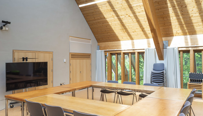 meeting room with wooden tables pushed together in a shape of a square with chairs surrounding it. there are large windows in the meeting room land the walls are painted blue