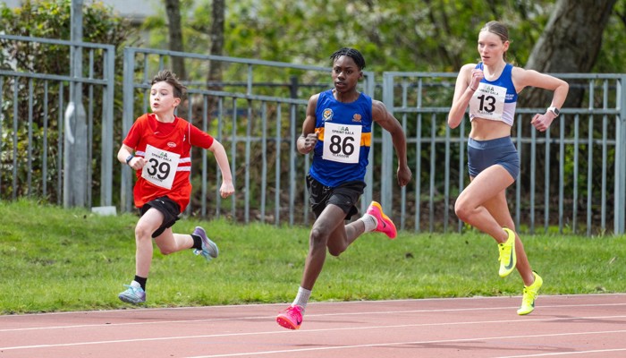 Three young sprinters, representing different age, genders and ethnicities, racing round the bend and into the straight during an athletics event.