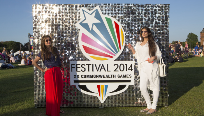 Two people posing in front of a shiny Festival 2014 board at Glasgow Green during the Commonwealth Games.