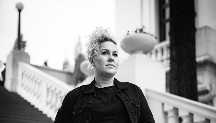 Irish musician Grainne Hunt standing at the bottom of an outdoor concrete staircase with her hand in her pocket.