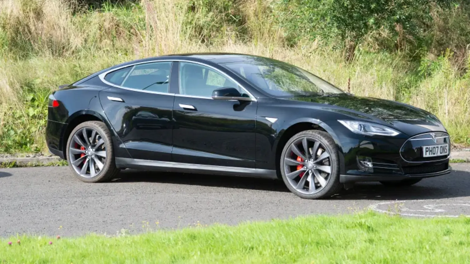 photo of a black Tesla electric car on a road among grass.