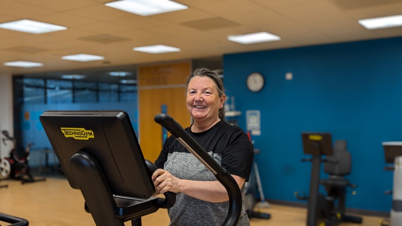 A picture of Glasgow Club member Anne-Marie Hanlon smiling while on the cross-trainer at Glasgow Club Emirates.