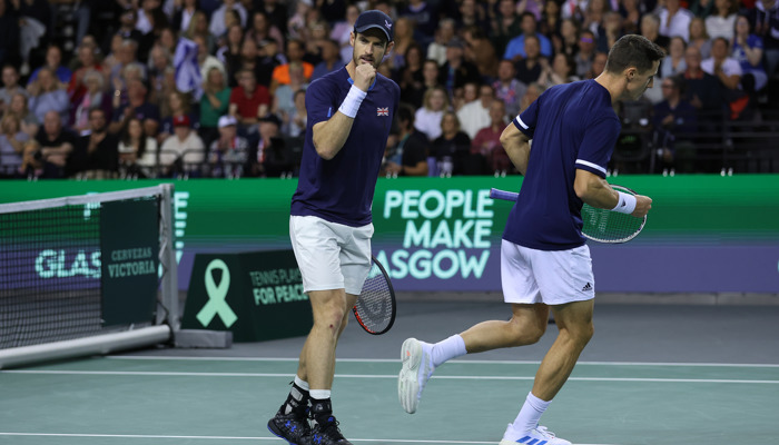 Andy Murray  on court clenching his fist during the Davis Cup at the Emirates Arena in 2022, behind him and his partner is a People Make Glasgow advertising hoarding.