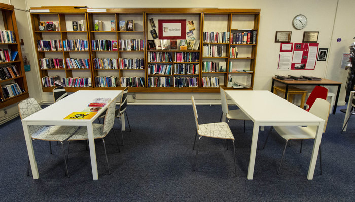 Two white rectangular tables in front of brown wooden bookshelves filled with books. 