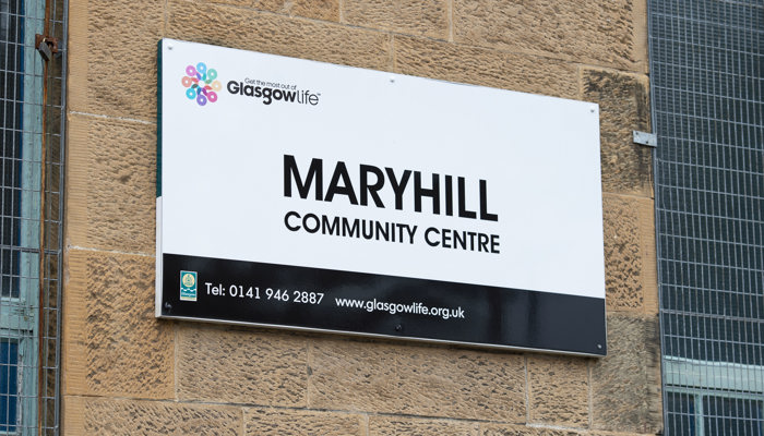 black and white sign that says maryhill community centre. it is attached to a brick wall outside the building