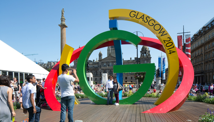 Two people getting their photo taken with the Big G sculpture on a sunny day in George Square during the Glasgow 2014 Commonwealth Games.