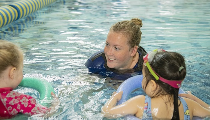 A swimming coach talking to two young children while in the pool