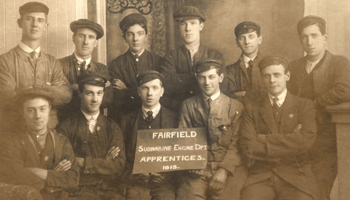 Black and white photo of 11 people sitting in dark uniforms, including hats and ties, holding a sign that says "Fairfield Submarine Engine Department Apprentices 1915"