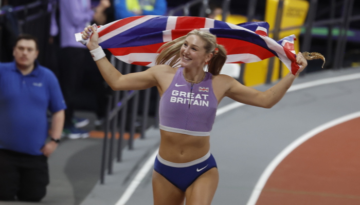 Team GB pole vaulter Molly Caudry on her victory lap in Glasgow after winning gold at the World Athletics Indoor Championships. She is wearing her Great Britain gear and is holding a union jack flag behind her.