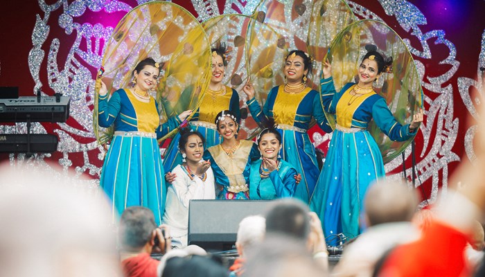 A group of dancers in colourful outfits performing on the main stage at the Glasgow Mela.