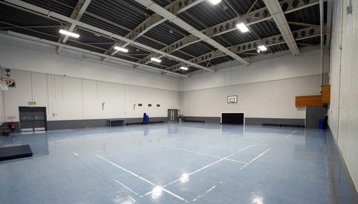 large sports room with marking on the ground for ball games. there is a basketball net on the far wall