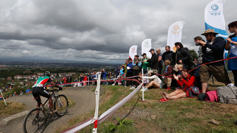 Crowds stand behind a rope at Cathkin Braes mountain trails during the Glasgow 2014 Commonwealth Games on a cloudy day.