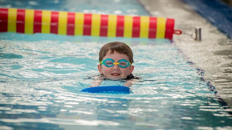 A child with goggles on smiling while in the water swimming with a float