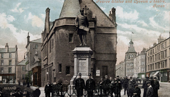 A photo of a theatre and statue in Glasgow with people posing outside them for the photo and other people just going about their day in the background.