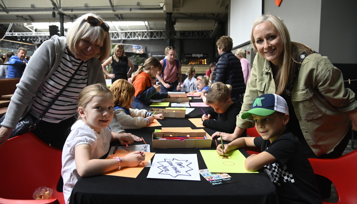 Young people sitting down and drawing or colouring in Merchant Square as part of GO LIVE events at the UCI Cycling World Championships. There are also two adults with the children.